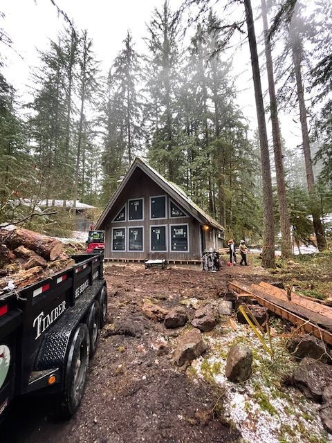 A dumpster is sitting in front of a house in the woods.