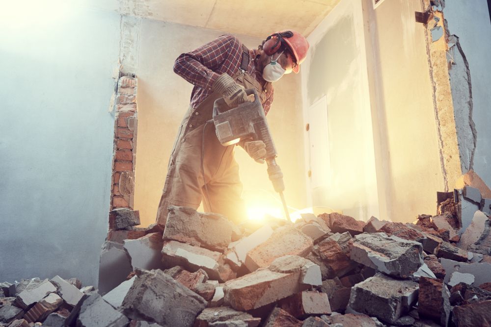 A construction worker is breaking bricks with a hammer.