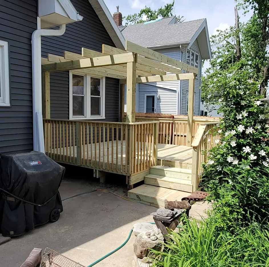 A wooden deck with a pergola and stairs is in the backyard of a house.