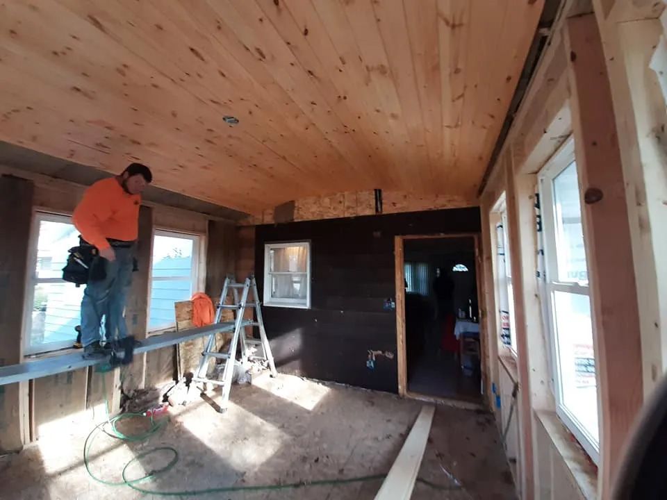 A man is standing on a ladder in a room with a wooden ceiling.