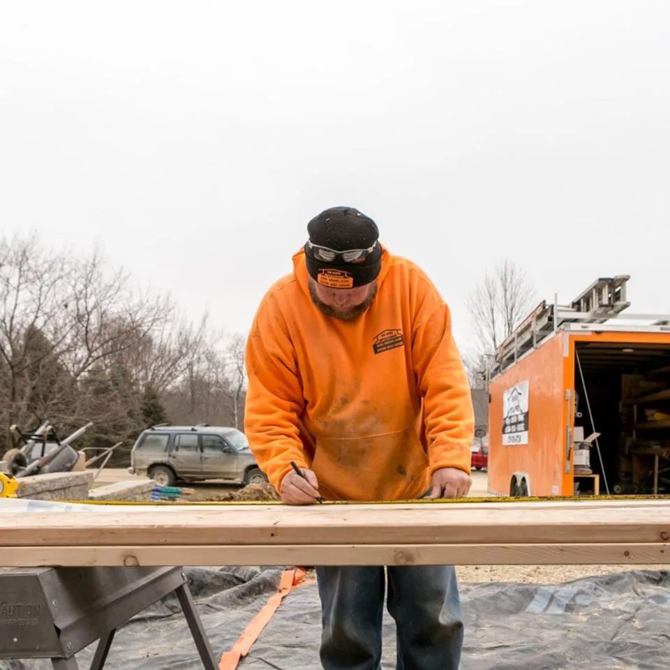 A man measuring a piece of wood with a tape measure