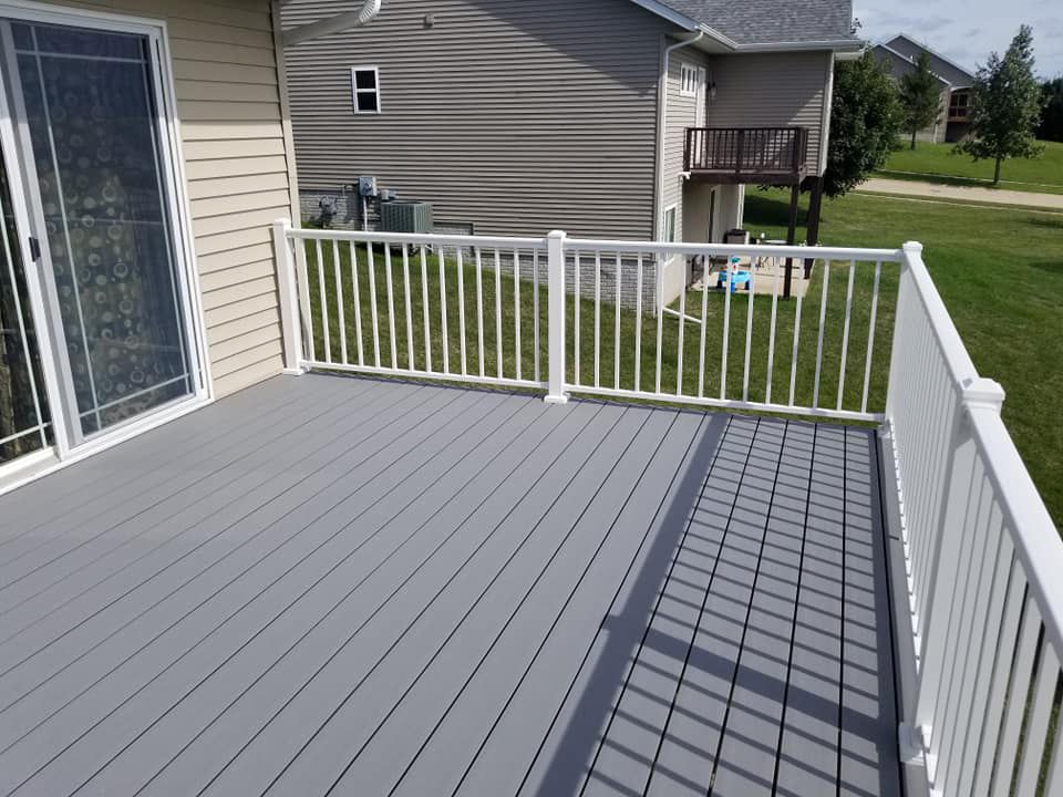 A gray deck with a white railing and a house in the background.