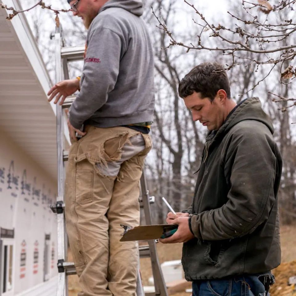 Two men are working on a house and one is writing on a clipboard.