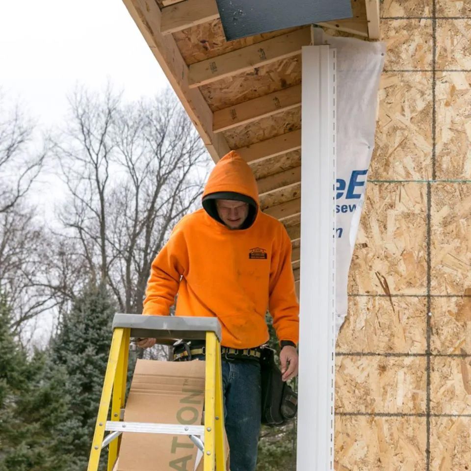A man wearing an orange hoodie is standing on a ladder