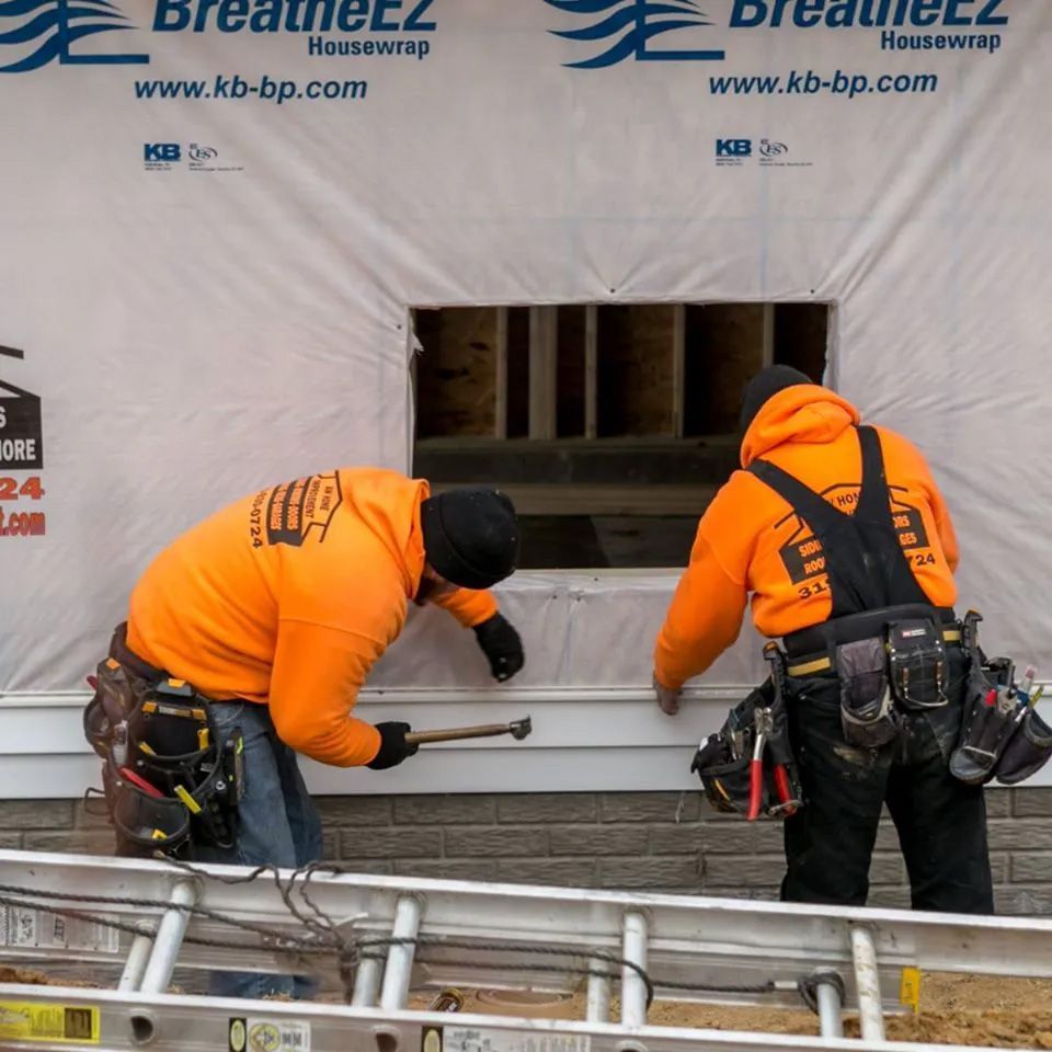 Two men wearing orange sweatshirts are working on a house