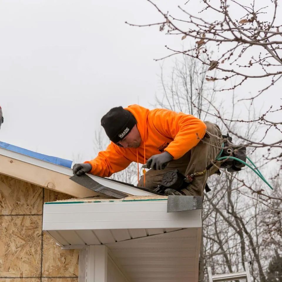 A man in an orange hoodie is working on a roof