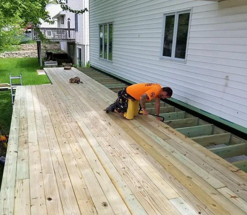 A man in an orange shirt is working on a wooden deck