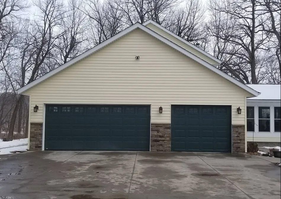 A large garage with three garage doors is sitting next to a house.