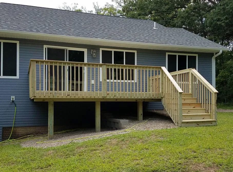 A blue house with a wooden deck and stairs in front of it.