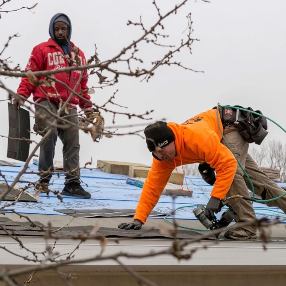 Two men are working on a roof with one wearing a red jacket that says cote