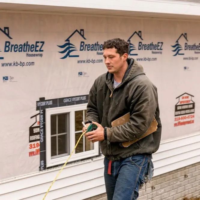 A man is measuring a window in front of a wall that says breatheez