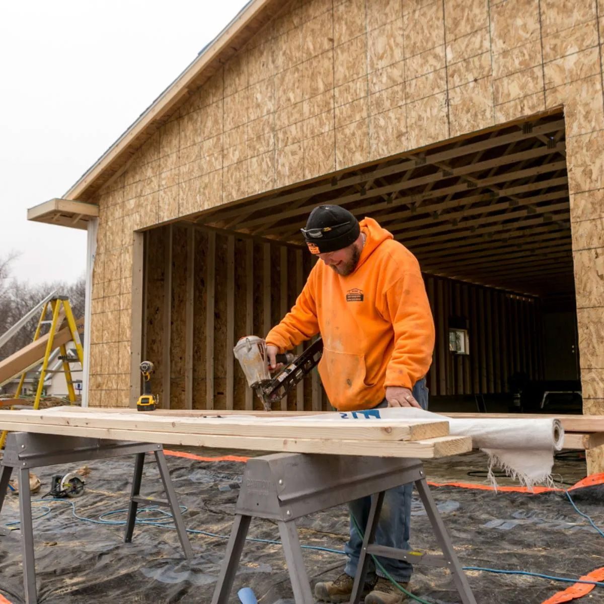 A man in an orange hoodie is working on a piece of wood