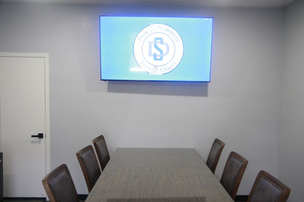 A conference room with a table and chairs and a television on the wall.