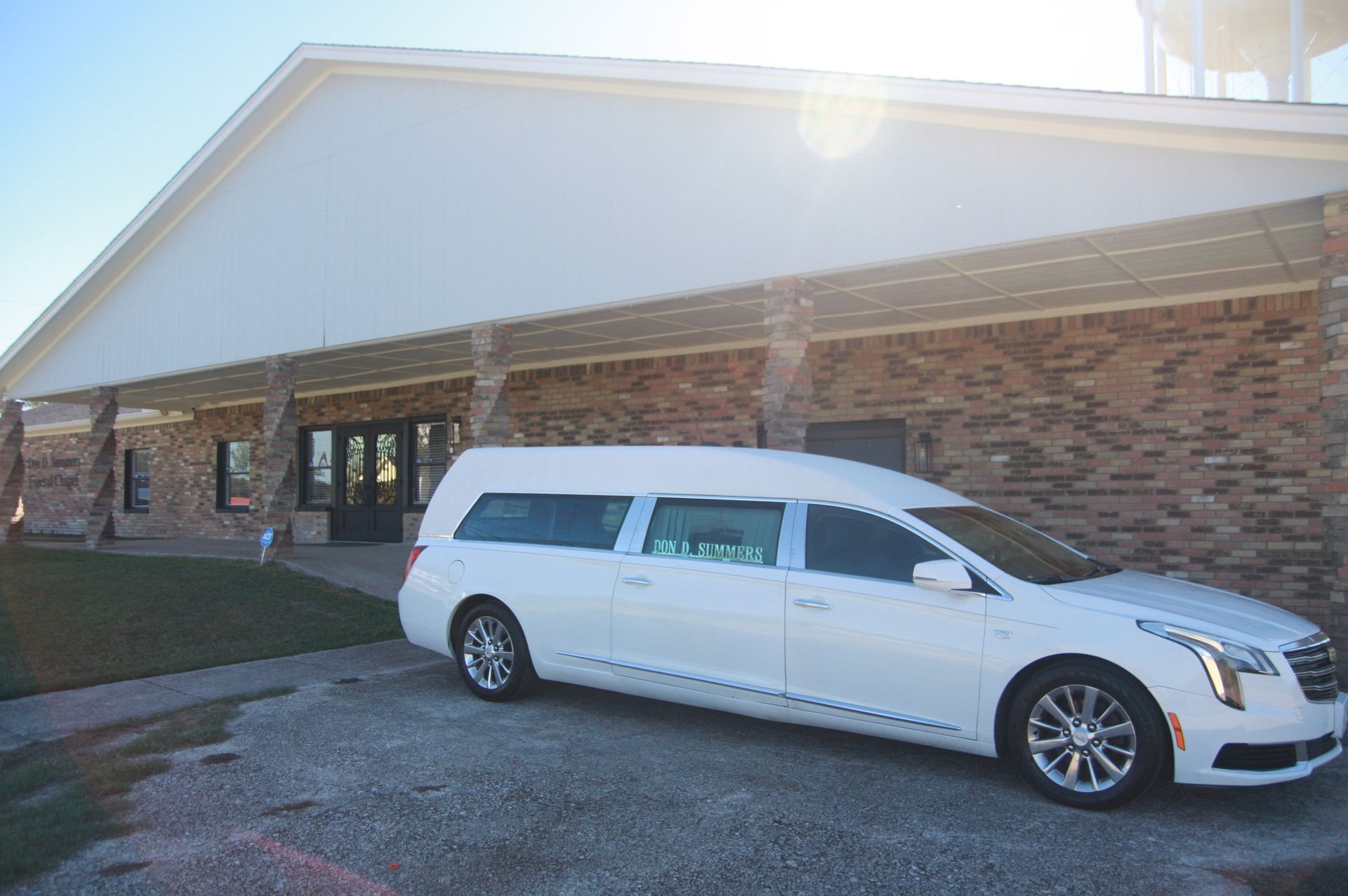 A white limousine is parked in front of a brick building.