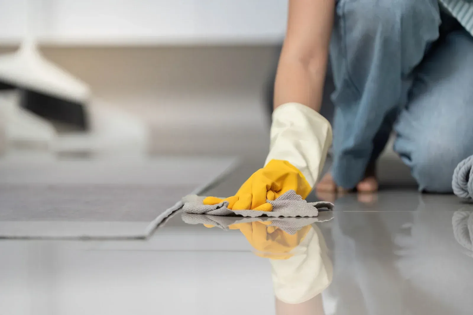 Person kneeling, wearing gloves, wiping a shiny, gray floor with a cloth.