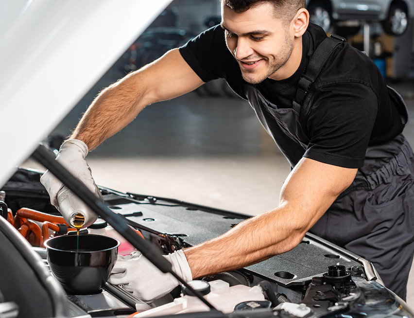 Mechanic pouring oil into a car engine, smiling in a garage. | King Mufflers