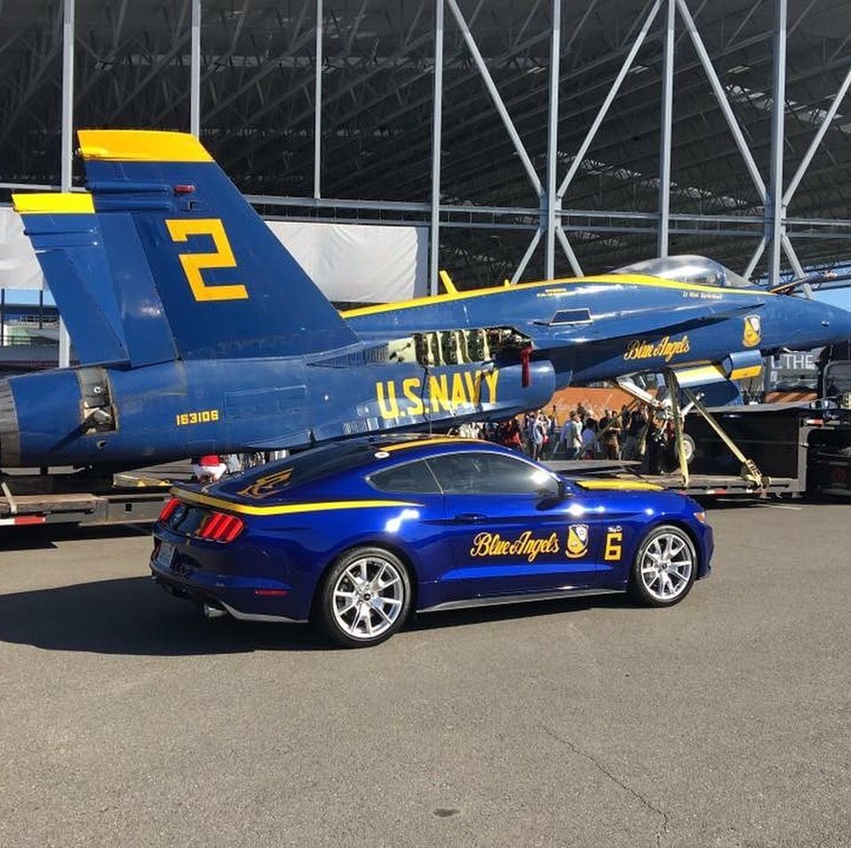 A blue u.s. navy jet is parked next to a blue car