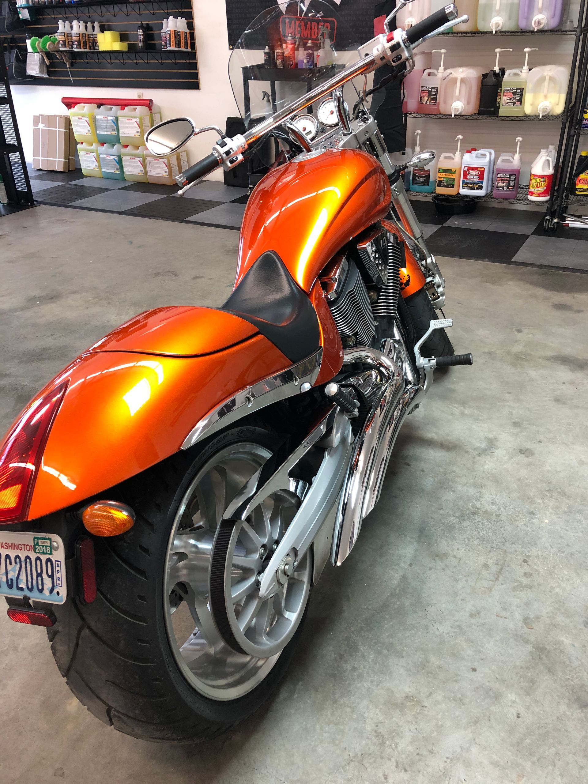 An orange motorcycle is parked in a garage with a california license plate