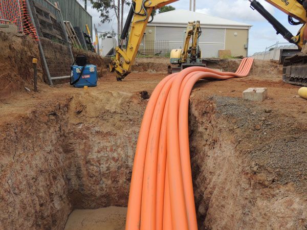 A bunch of orange pipes are laying in the dirt.