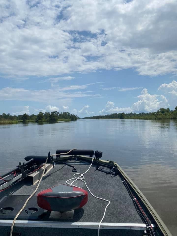 Boat traveling on calm water, surrounded by marshland under a partly cloudy sky.