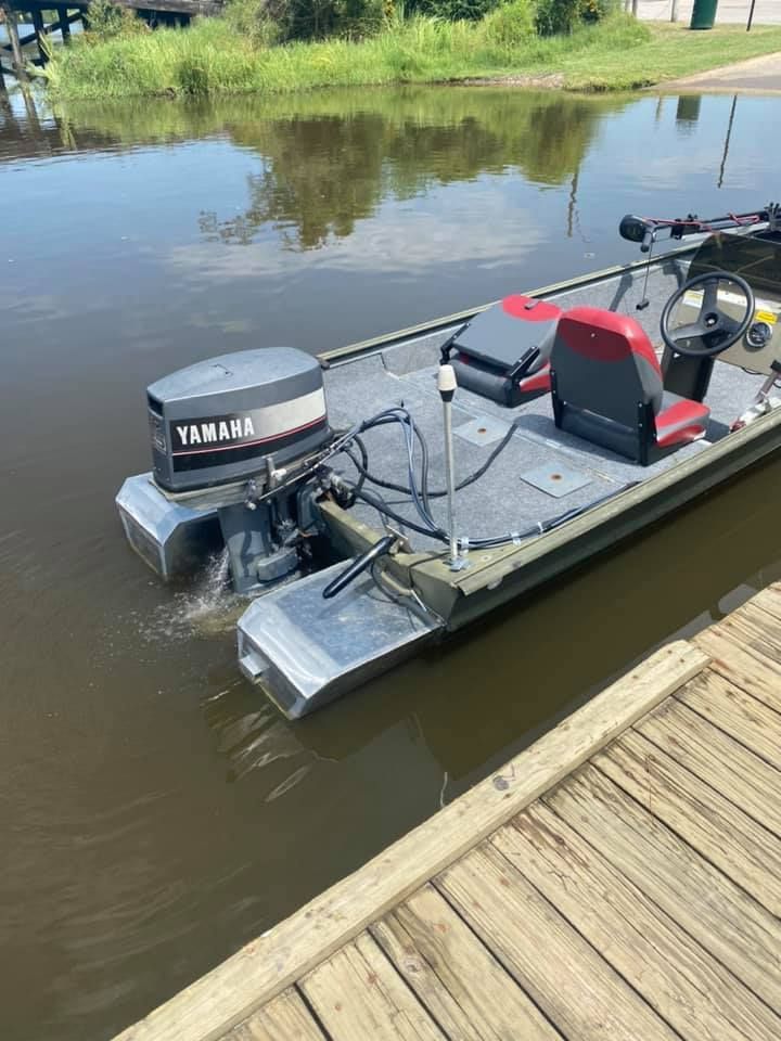 A small boat with a Yamaha motor is docked near a wooden pier. The motor is running, creating a wake.