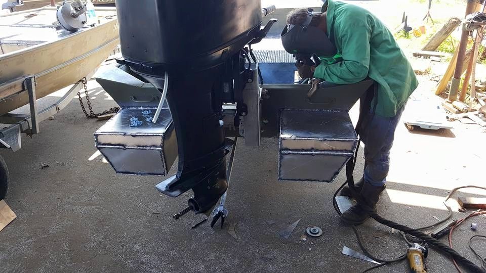 Person welding metal boat components, wearing protective gear. Outdoors, daytime.