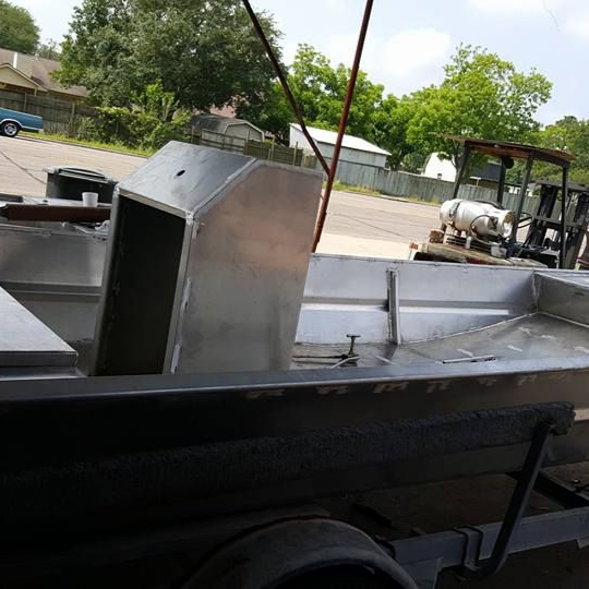 Aluminum boat under construction with welding and trailer visible.