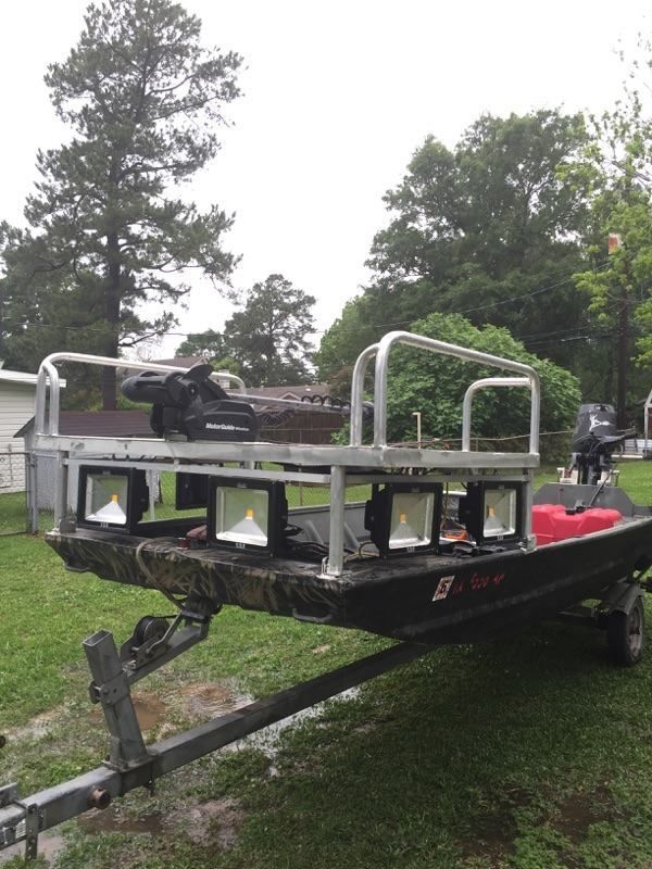 A flat-bottomed boat on a trailer, with a platform holding spotlights and rails. Outdoors, overcast day.