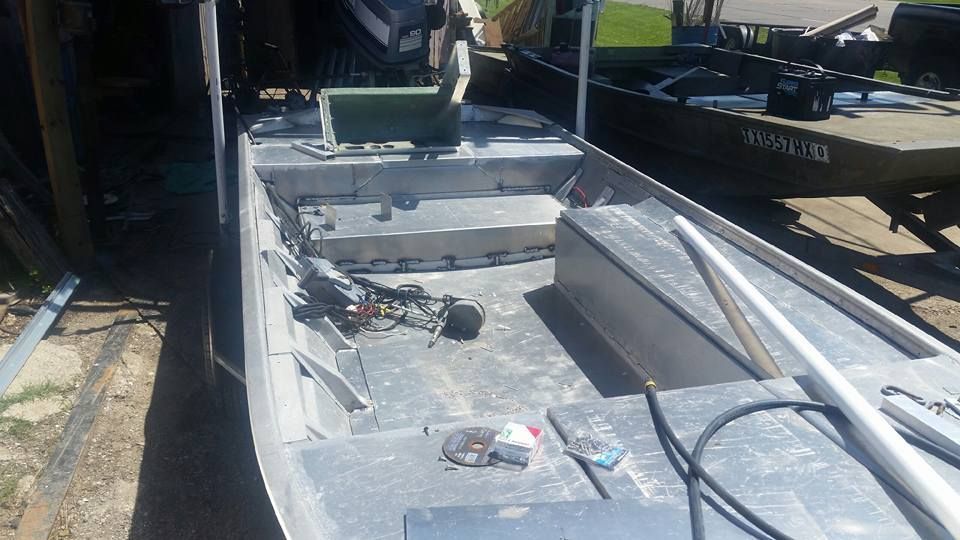 Aluminum boat interior; bench seat, storage compartments, various tools/parts. Outdoor setting.