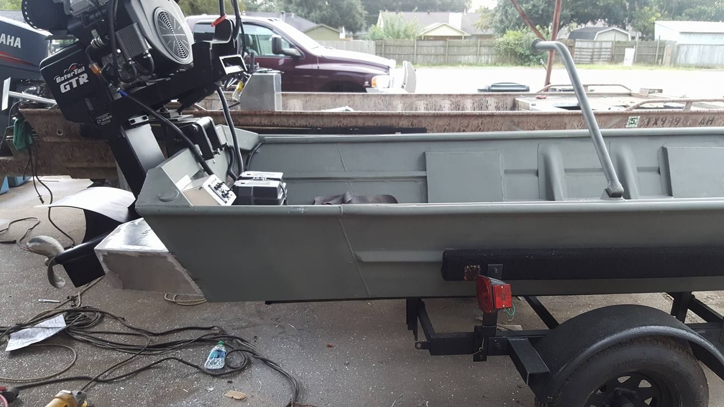 Green metal boat on trailer with outboard motor attached.