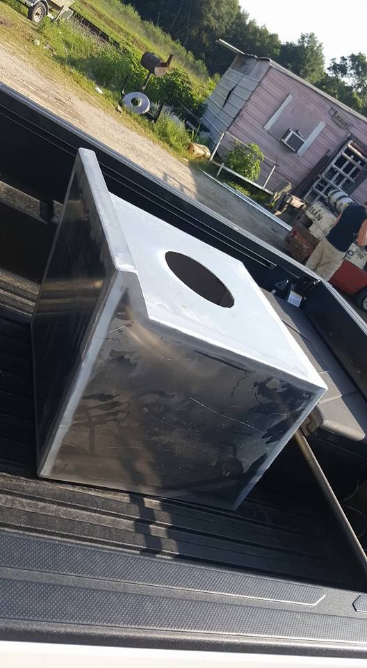 Shiny metal box with a circular opening, possibly a trash receptacle, in a truck bed outdoors.