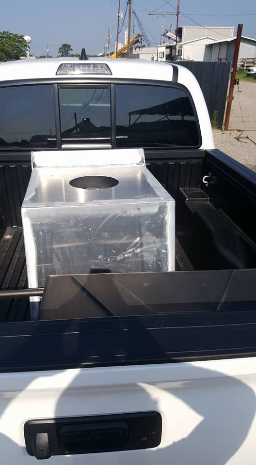 White pickup truck bed carrying a large, metal, box-shaped structure, possibly equipment.