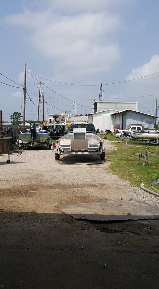 Boat on trailer parked in a lot, with buildings and utility poles in the background under a cloudy sky.