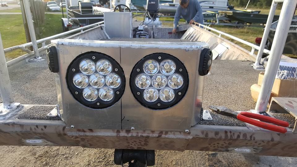 Aluminum boat with two large LED lights mounted on the front; a person works in the boat.