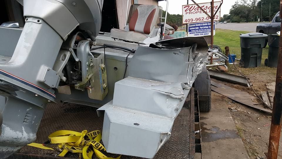 Damaged silver boat on trailer, side view, with outboard motor and seats.
