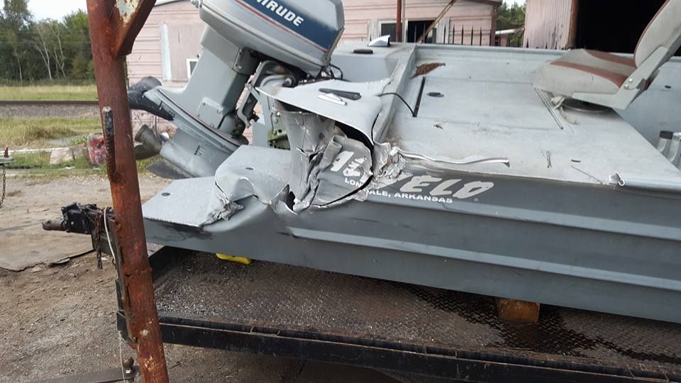 Damaged gray metal boat with outboard motor, on a trailer. Significant dent in the side.