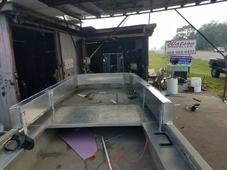 Inside a partially constructed aluminum boat, outdoors under a metal awning at a business.