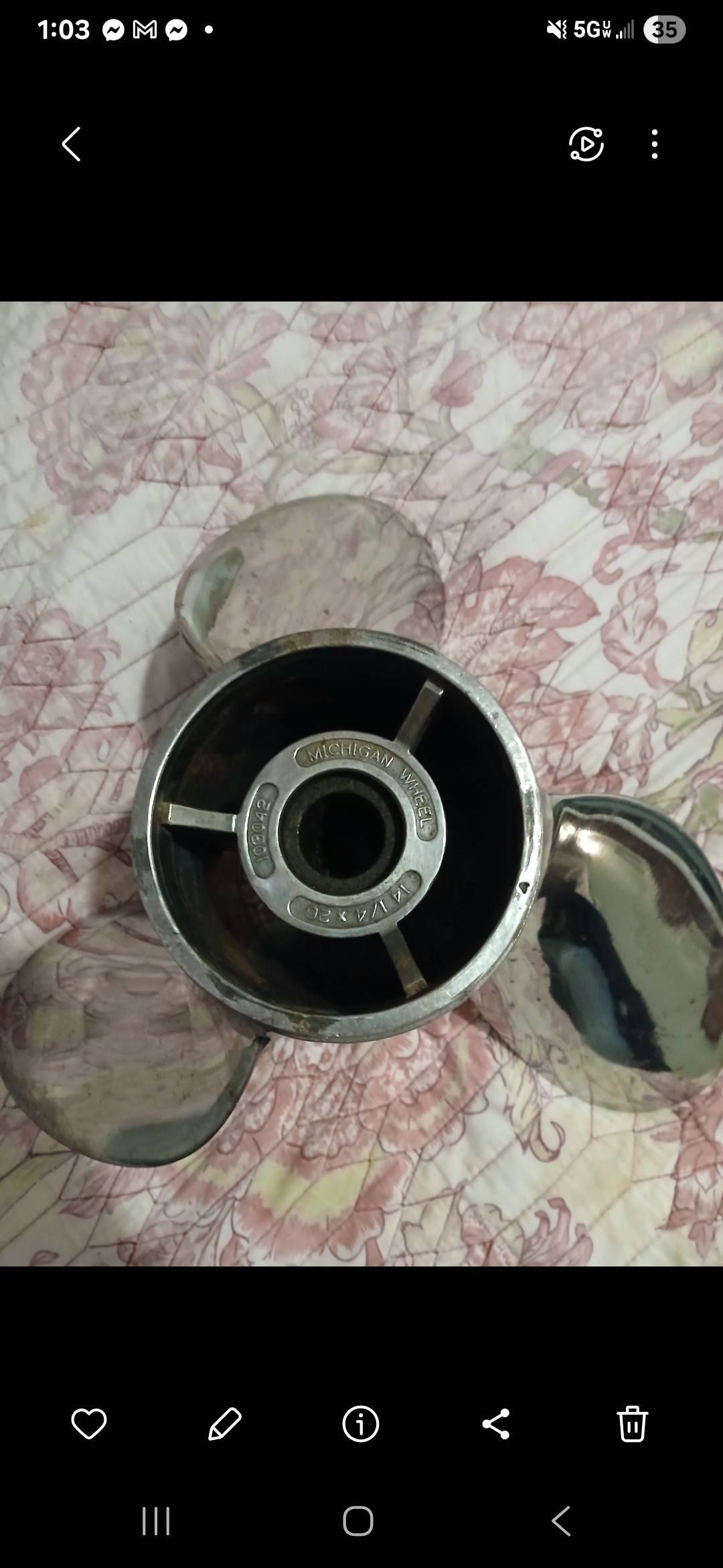 A shiny boat propeller with three blades on a floral patterned surface.