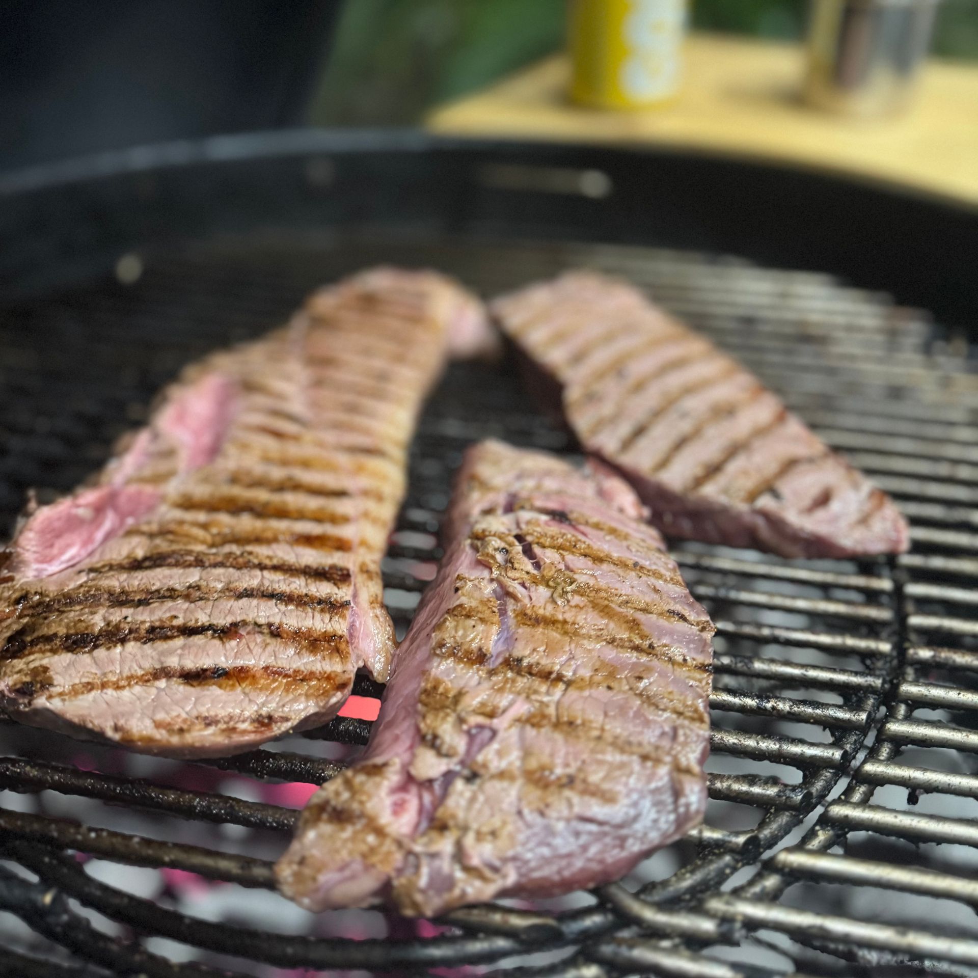 Three steaks grilling on a charcoal grill, with grill marks and pink interiors.