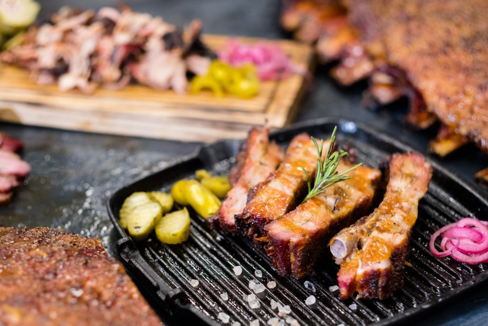 Grilled ribs on a griddle, with other BBQ meats, pickles, and onions.