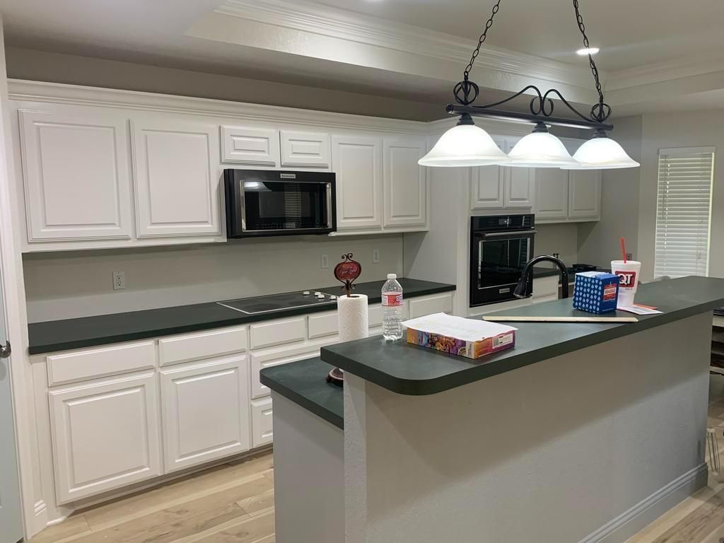 A kitchen with white cabinets , black counter tops , and a microwave.