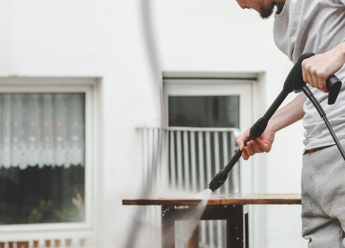 A man is cleaning a wooden table with a high pressure washer.