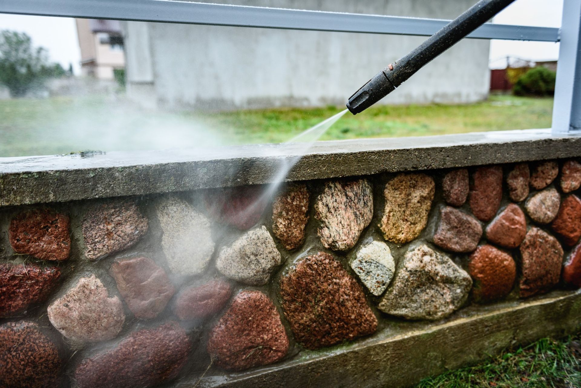 A person is using a high pressure washer to clean a stone wall.