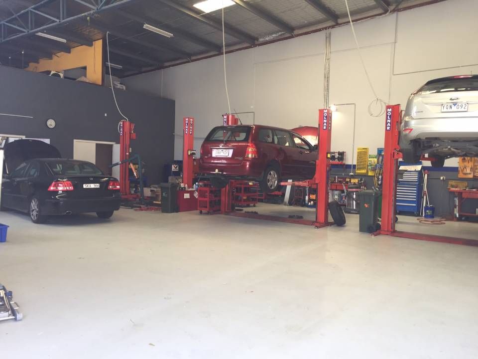 Auto repair shop with cars on lifts and a black sedan parked inside
