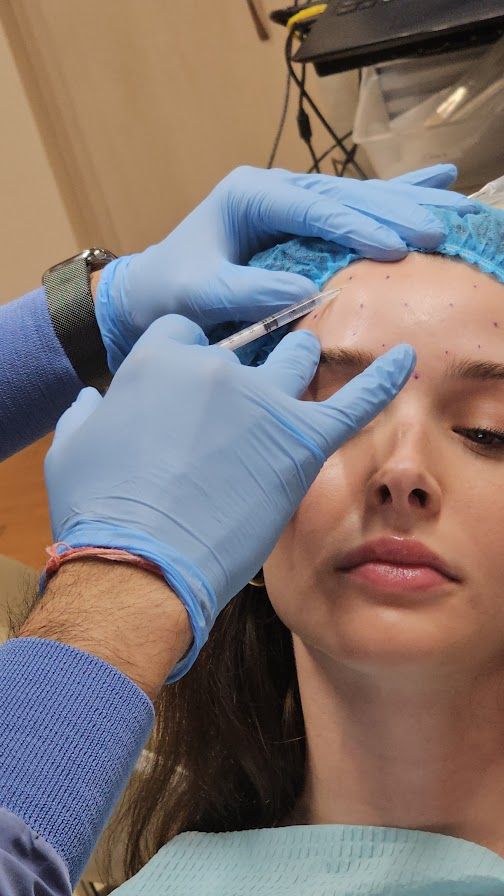 Dentist examining a patient's face in an office setting. Both are wearing masks and gloves.