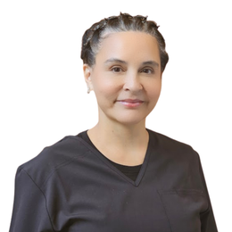 Woman in black scrubs, smiling, looking at the camera. Neutral background.