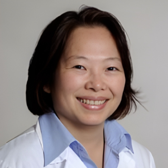 Woman smiling, wearing a white lab coat with a light blue collared shirt.