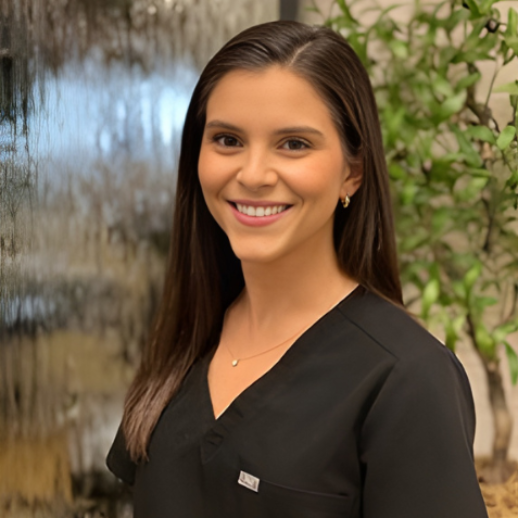 Woman in black scrubs smiling, near a water feature and greenery.