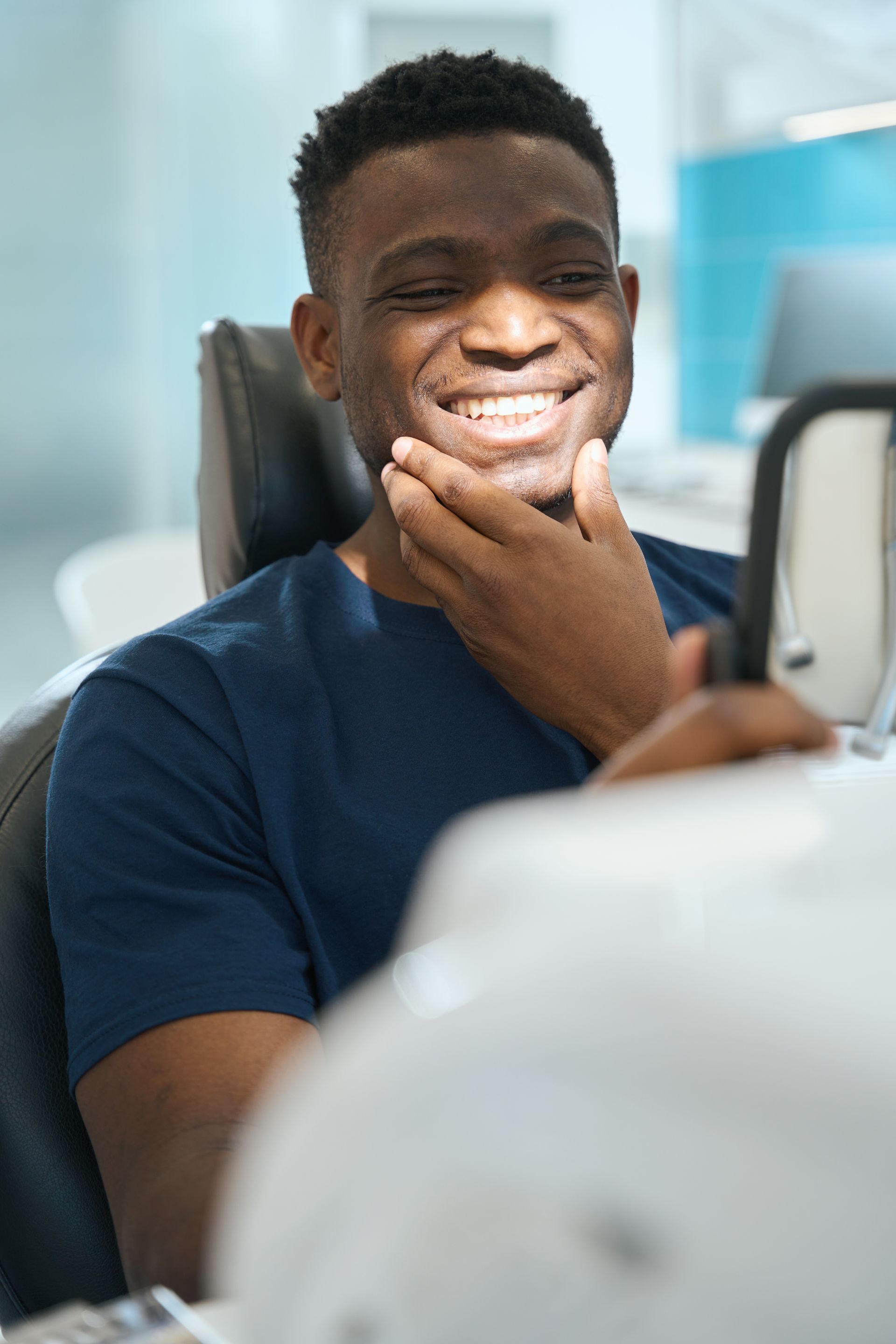 Man smiles, checking his teeth in a mirror at a dentist's office.