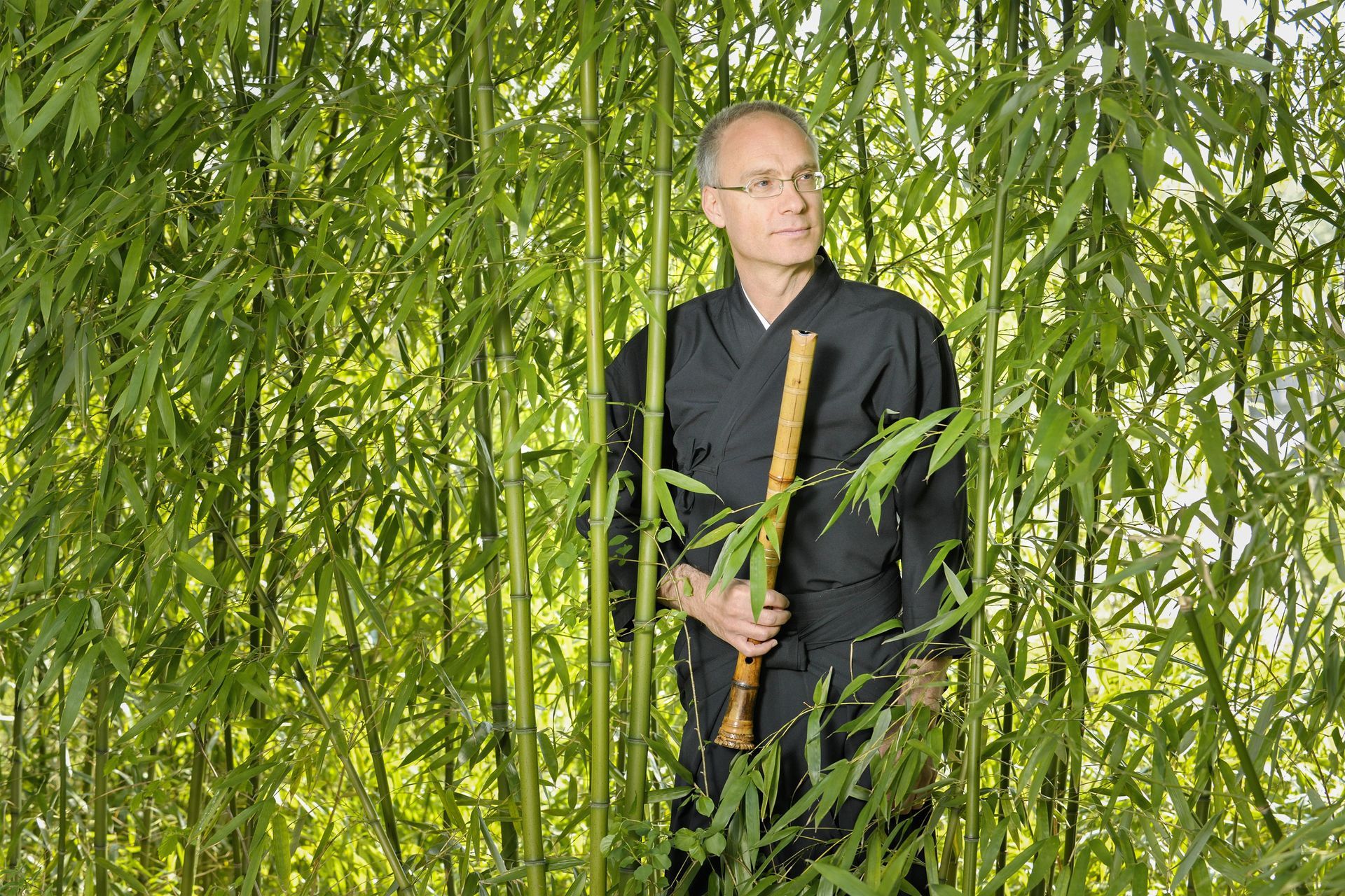 Jürg im Kinono hält eine Bambusflöte und steht in einem Bambushain.